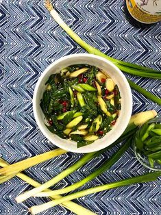 a white bowl filled with green vegetables next to two wine bottles on top of a blue and white table cloth