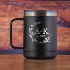 a black coffee mug with the initials and date on it, sitting on a wooden table