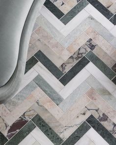 an upholstered chair sits in front of a chevron marble tile floor that looks like herringbones