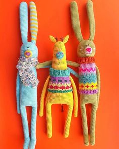 three crocheted stuffed animals sitting next to each other on an orange background,