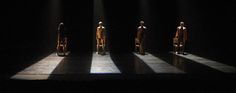 four wooden mannequins standing in the dark with their shadows cast on them