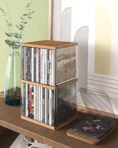 a stack of dvd's sitting on top of a table next to a vase with flowers