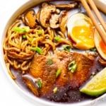 a bowl filled with noodles, meat and vegetables next to chopsticks on a white surface