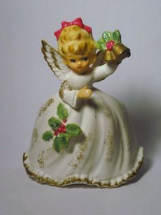 an angel figurine holding a bell with holly berries on it's side