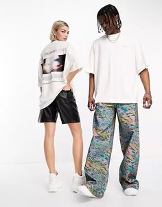 two people standing next to each other in front of a white wall wearing colorful pants and t - shirts