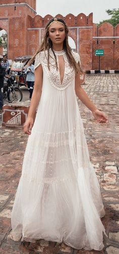 a woman in a long white dress standing on a brick walkway with people behind her