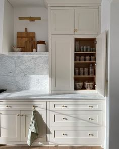 a kitchen with white cabinets and marble counter tops in the center is an open cupboard