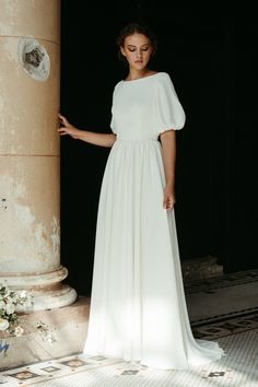 a woman in a white dress standing next to a pillar