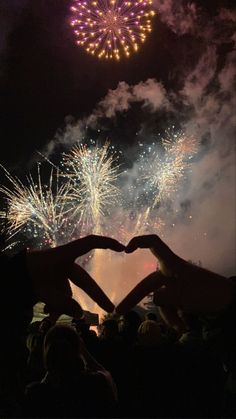 two people making a heart with their hands in front of fireworks