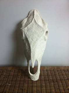 a white sculpture sitting on top of a wicker table next to a gray wall