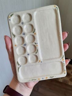 a hand holding a ceramic tray with holes in it