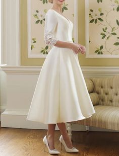 a woman standing in front of a couch wearing a white dress