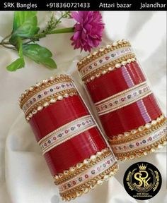 two red and gold bangles with white pearls on the ends, sitting next to a purple flower