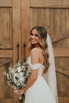 a woman in a wedding dress holding a bouquet of flowers and smiling at the camera