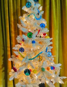 a white christmas tree decorated with peace signs and other ornaments in front of a yellow curtain