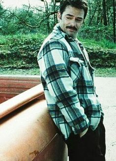 a man leaning on the back of a pickup truck with his hands in his pockets