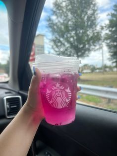 a person holding up a pink drink in their car