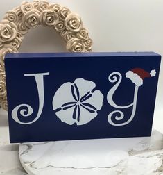 a wooden sign with the word joy written in white on a blue background next to a wreath