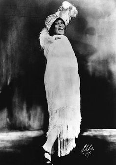 an old black and white photo of a woman wearing a dress with feathers on it