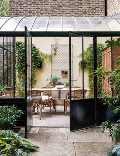 an enclosed patio with tables and chairs in the middle of it, surrounded by greenery