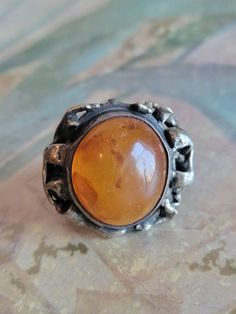 This is a vintage, hand made sterling silver and amber (I'm not certain if it's real amber or not) ring. The amber is round in shape, orange in color and domed, but the top is uneven and has some natural flaws. It has tested positive for sterling silver. All sales are final. This ring is a size 7 and can be sized. Please note, sizing is up to the buyer. I do not provide this service. If you have a wish list or are looking for something specific, please ask. I may have exactly what you are looking for. As always please convo me with any questions or concerns regarding this item or with any international shipping questions. Unfortunately I do not accept returns or grant refunds. All shipping fees include handling fees. If you would like to combine shipping costs for more than one item, I wou Antique Amber Cabochon Rings, Antique Amber Rings For Collectors, Spiritual Amber Cabochon Ring, Vintage Amber Oval Cabochon Ring, Antique Amber Round Ring, Vintage Oval Cabochon Amber Ring, Vintage Orange Rings For Collectors, Vintage Orange Cabochon Rings, Handmade Vintage Orange Rings