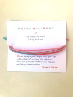 a red string bracelet with the words happy birthday on it and a card attached to it