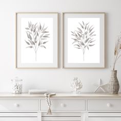 two framed art prints sitting on top of a white dresser