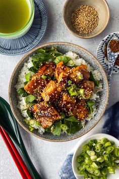 a bowl filled with chicken and rice next to chopsticks, bowls of green onions and sesame seeds