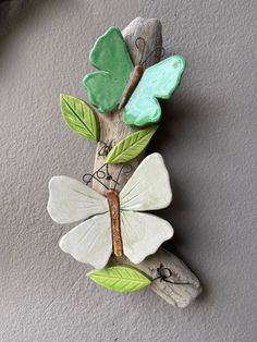 a wooden branch with green leaves and a butterfly on it's back, attached to the wall