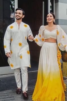 two people dressed in white and yellow outfits walking down the street with sunflowers on them