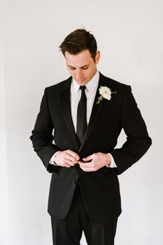 a man in a tuxedo adjusts his tie