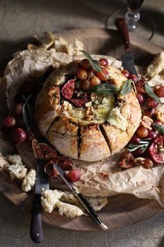 bread with olives, tomatoes and other toppings on a wooden platter next to utensils