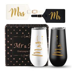 two black and white wine tumblers with gold lettering on them, next to a gift box