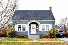 a blue house with a white door and windows in the front yard next to a black car