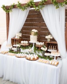 a table topped with cakes and cupcakes under a white drape covered curtain