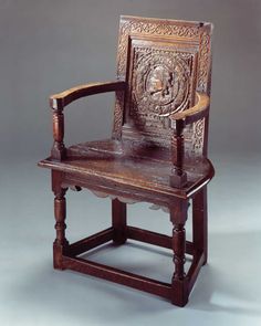 an old wooden chair with carvings on the back and arm rests against a gray background