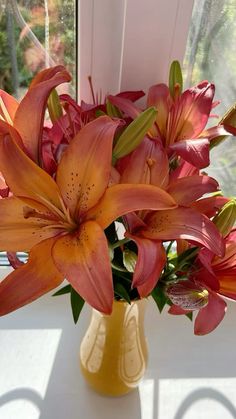 a yellow vase filled with orange lilies on top of a window sill next to a window