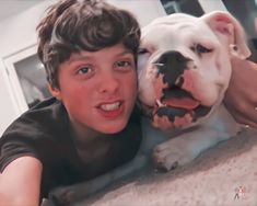 a young boy laying on the floor with his dog, who is smiling at the camera