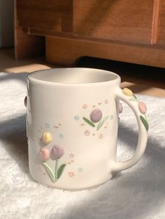 a white coffee cup with flowers painted on the outside and inside, sitting on a bed