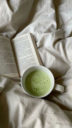 a cup of green tea and an open book on a bed