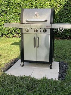 a grill sitting on top of a cement slab in front of some grass and bushes