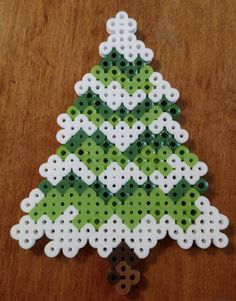 a green and white christmas tree made out of perforded beads on a wooden table