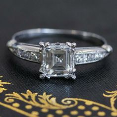 an engagement ring with a princess cut diamond in the center and side stones on each band