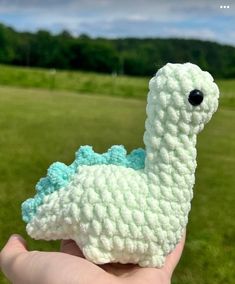 a hand holding a small crocheted llama in the middle of a field