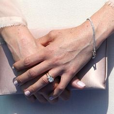 two hands holding each other on top of a pink bag with a diamond ring in it