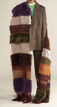 a man in a suit and scarf standing next to a pile of knitted material