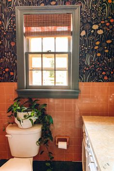 there is a potted plant sitting on the toilet in this bathroom with floral wallpaper