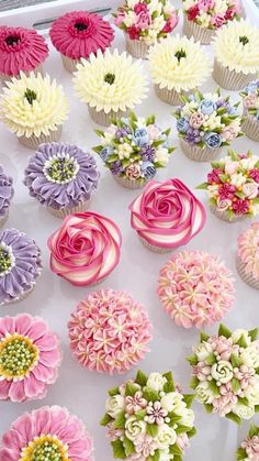 cupcakes decorated with pink, white and purple flowers are on display in a box