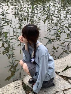 a woman sitting on the edge of a body of water with her head in her hands