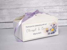 a white box with a purple ribbon tied around it and a flower on the front